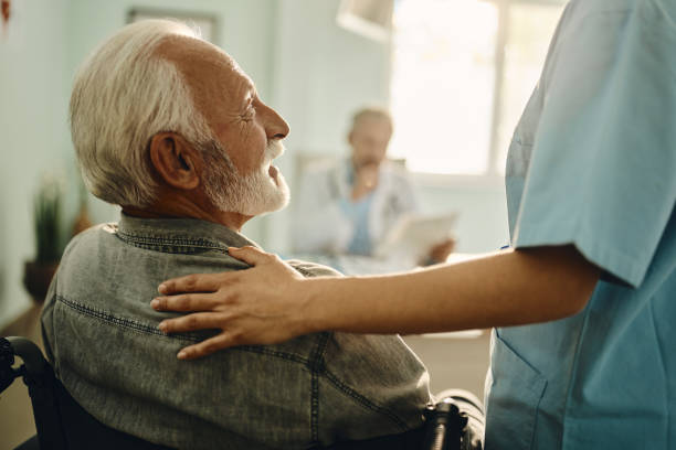 Pflegefachkraft im Gespräch mit einem älteren Patienten im Rollstuhl